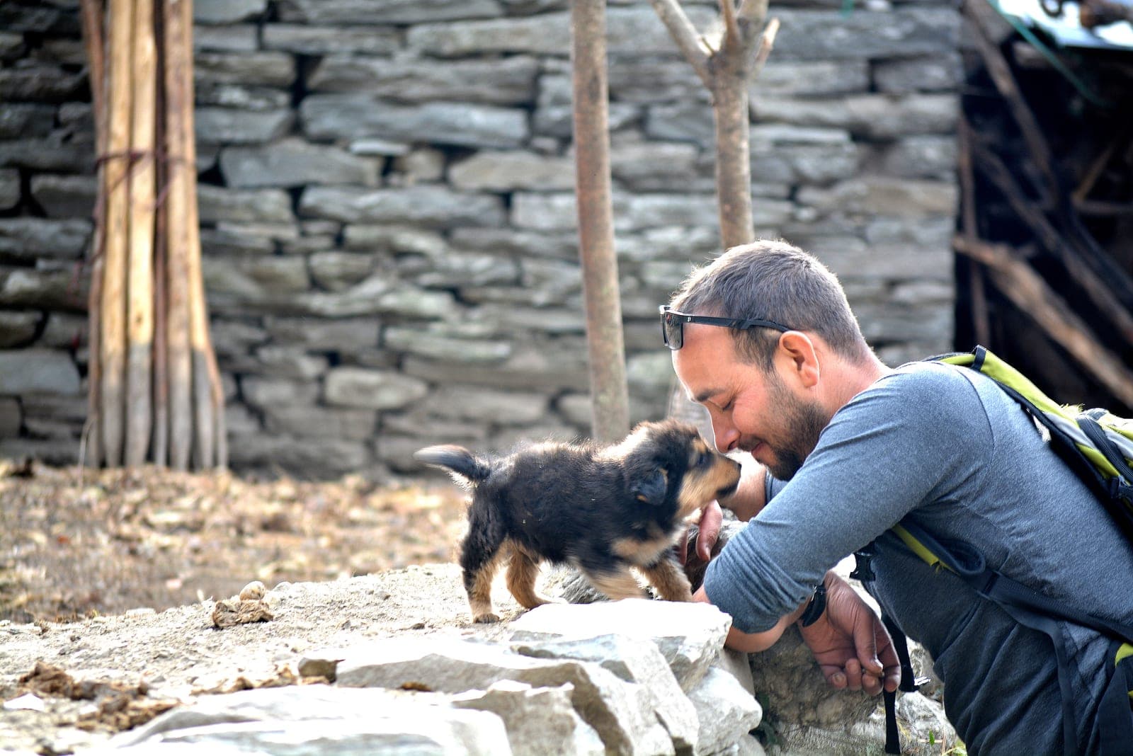 Bhuwan crouching to greet a puppy on a stone wall in a trail village